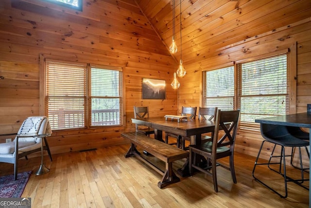 dining space with light wood-type flooring, wood walls, and high vaulted ceiling