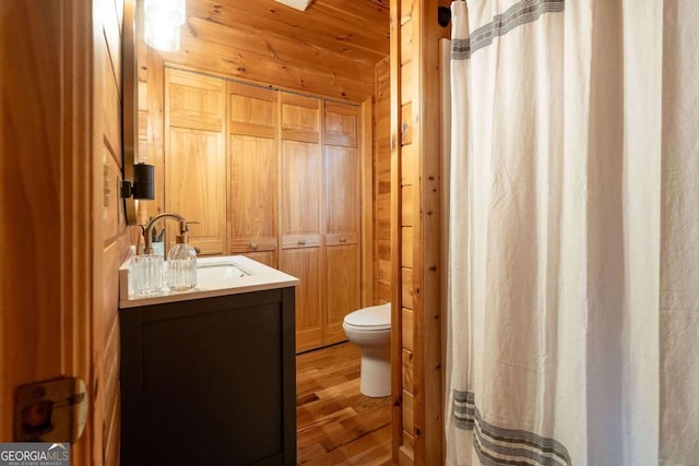 full bath with wooden walls, a shower with shower curtain, toilet, wood finished floors, and vanity