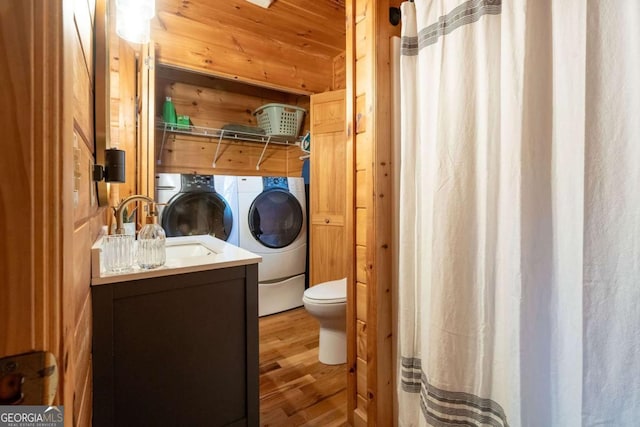 bathroom featuring toilet, separate washer and dryer, wood walls, wood finished floors, and vanity