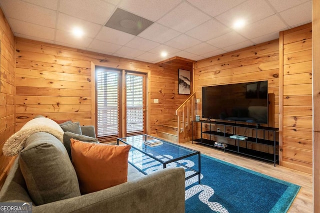 living room featuring stairs, a drop ceiling, wood finished floors, and wooden walls