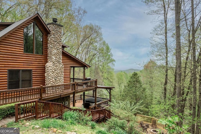 view of property exterior with log veneer siding, a chimney, a forest view, and a wooden deck