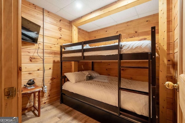 bedroom with wood finished floors, a paneled ceiling, and wooden walls