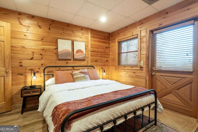 bedroom with light wood-type flooring, a paneled ceiling, and wooden walls