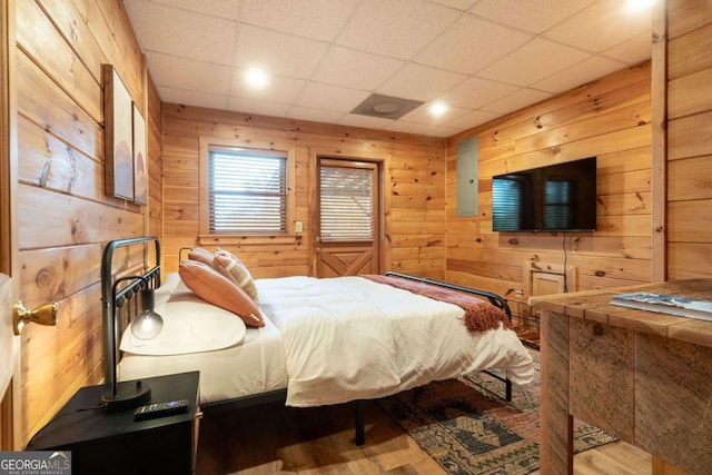 bedroom with a paneled ceiling, wood walls, and wood finished floors