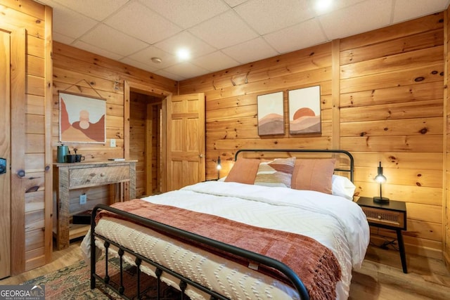 bedroom with a paneled ceiling, light wood-style flooring, and wooden walls