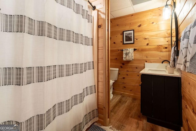 full bathroom with a paneled ceiling, curtained shower, toilet, wooden walls, and wood finished floors