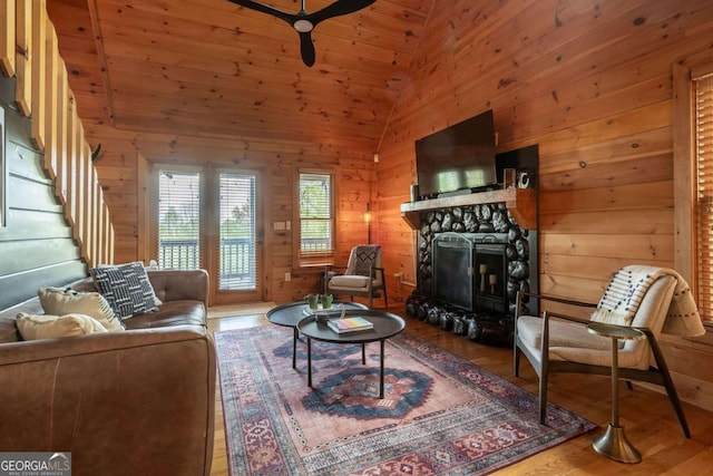 living area featuring wood-type flooring, stairway, vaulted ceiling, a stone fireplace, and wood walls