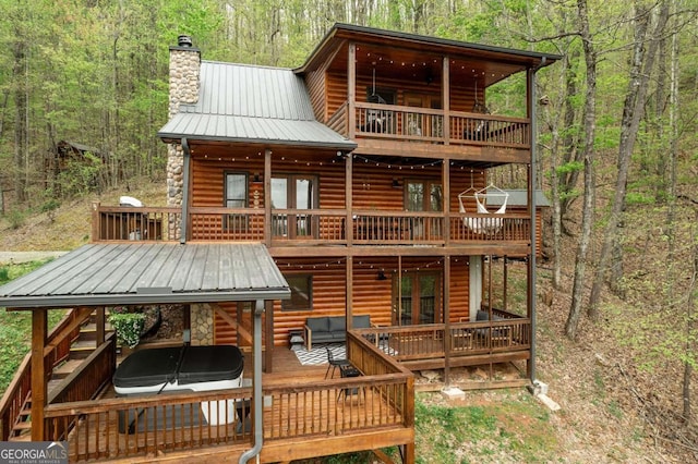 back of property with a chimney, a deck, and a wooded view