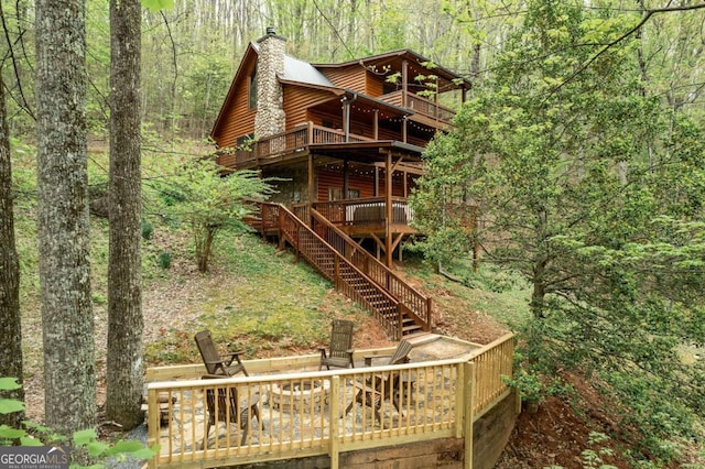 rear view of house with a fire pit, stairway, a wooded view, and faux log siding