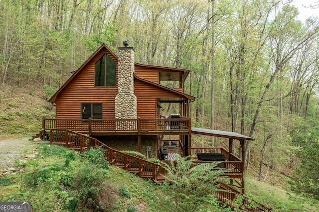 exterior space featuring a forest view, a chimney, a deck, and log veneer siding