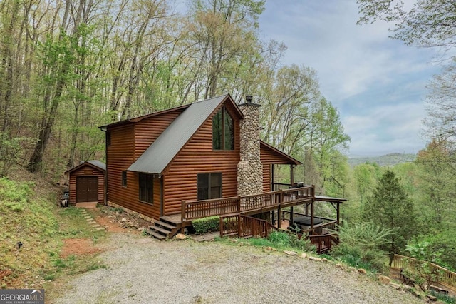 view of property exterior featuring a chimney, metal roof, a deck, a wooded view, and faux log siding