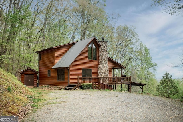 exterior space featuring a deck, a storage shed, an outdoor structure, faux log siding, and a chimney