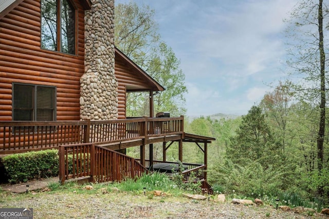 view of side of property with a deck, log veneer siding, and a chimney