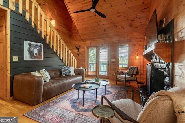 living room with a fireplace with raised hearth, light wood-style flooring, a ceiling fan, wooden walls, and wooden ceiling