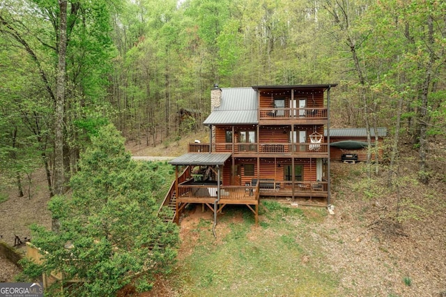 rear view of house with a deck, metal roof, log veneer siding, a chimney, and a wooded view