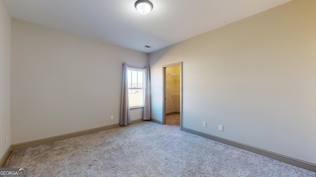 interior space with a walk in closet, light carpet, visible vents, and baseboards