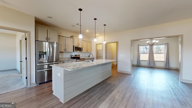 kitchen featuring light stone counters, stainless steel appliances, wood finished floors, a sink, and an island with sink