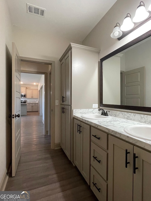 bathroom featuring double vanity, visible vents, a sink, and wood finished floors