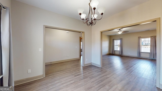 spare room featuring ceiling fan with notable chandelier, baseboards, and wood finished floors