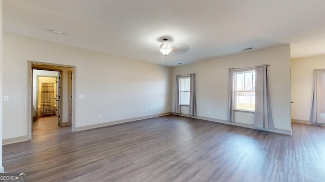 unfurnished room with ceiling fan, wood finished floors, visible vents, and baseboards