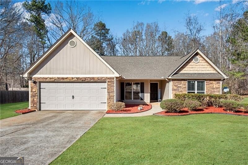 view of front facade with driveway, stone siding, a garage, and a front yard