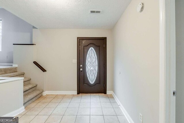 foyer with light tile patterned floors, visible vents, a textured ceiling, and stairs