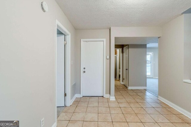 empty room featuring baseboards, visible vents, a textured ceiling, and light tile patterned flooring