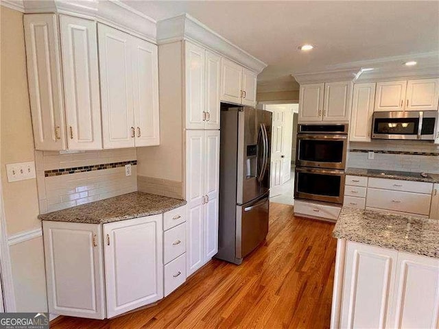 kitchen featuring stainless steel appliances, tasteful backsplash, light wood-style flooring, and white cabinets