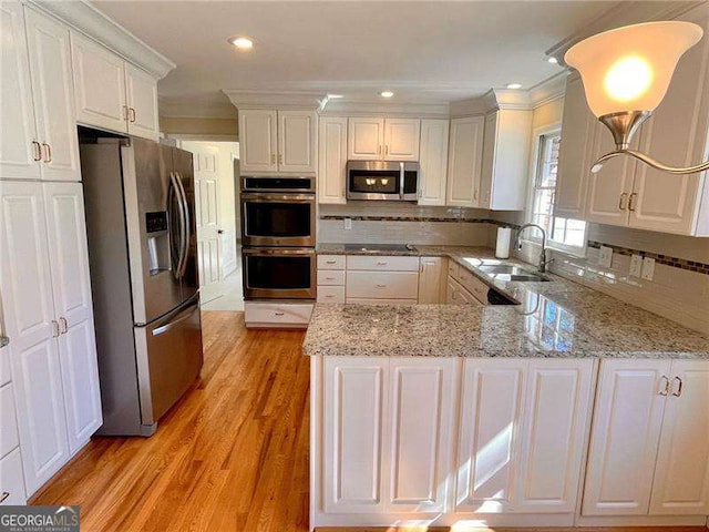 kitchen with a sink, stainless steel appliances, light wood-type flooring, white cabinetry, and backsplash