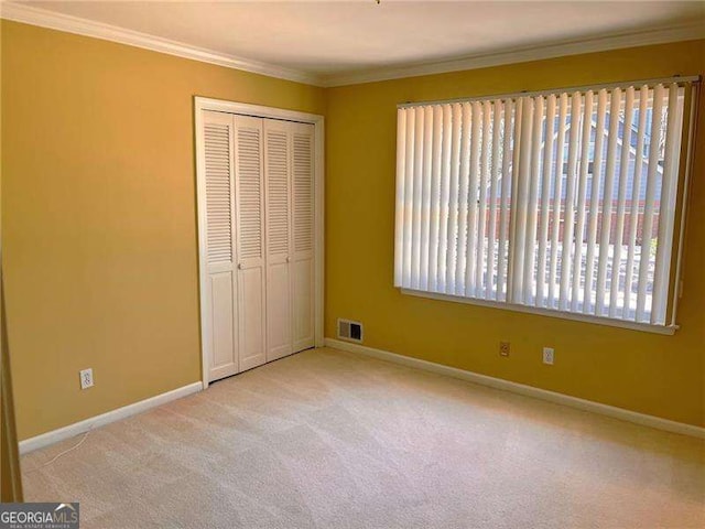 unfurnished bedroom featuring baseboards, visible vents, crown molding, carpet floors, and a closet