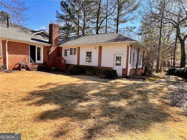 view of home's exterior with brick siding, a chimney, a lawn, entry steps, and fence