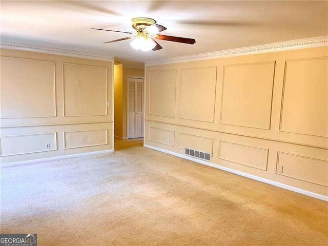 unfurnished bedroom featuring light colored carpet, a decorative wall, visible vents, a ceiling fan, and crown molding