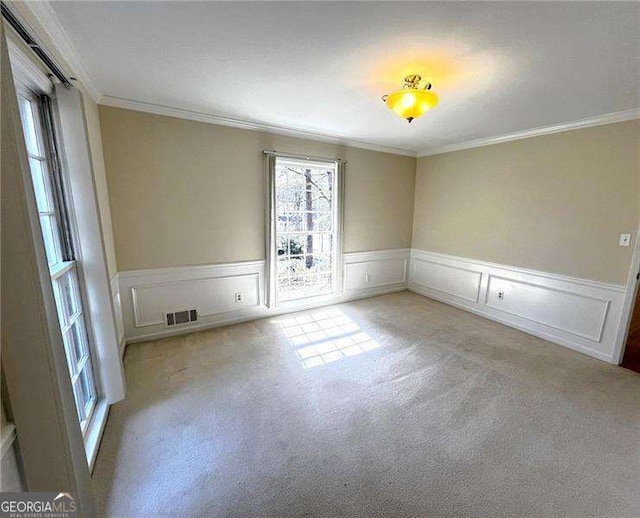 spare room with carpet floors, wainscoting, visible vents, and crown molding