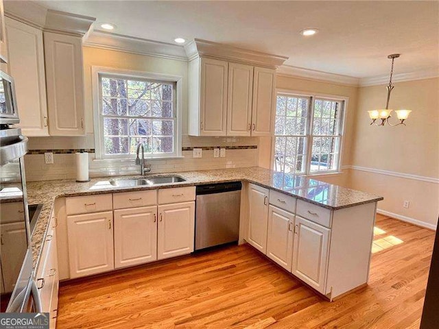 kitchen featuring a peninsula, a sink, stainless steel dishwasher, light wood-type flooring, and crown molding