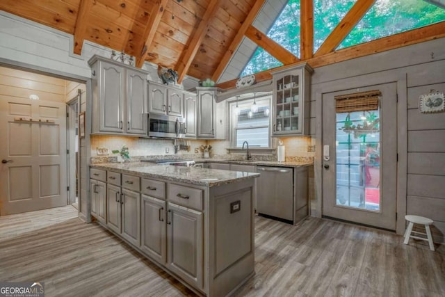 kitchen with glass insert cabinets, vaulted ceiling with beams, stainless steel appliances, light wood-type flooring, and a sink