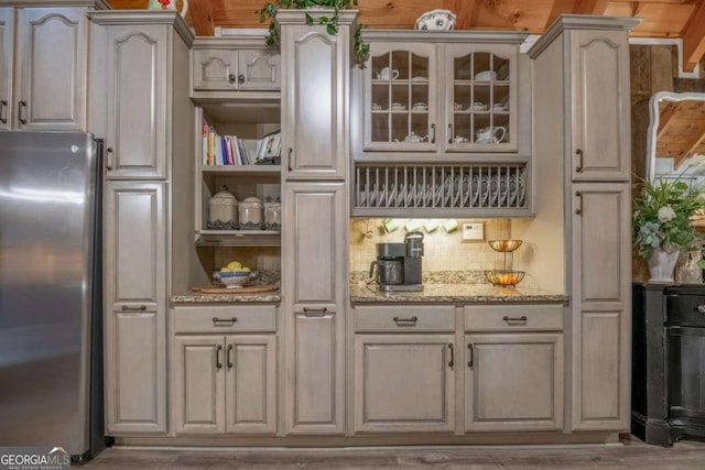 kitchen with glass insert cabinets, light stone countertops, freestanding refrigerator, and decorative backsplash