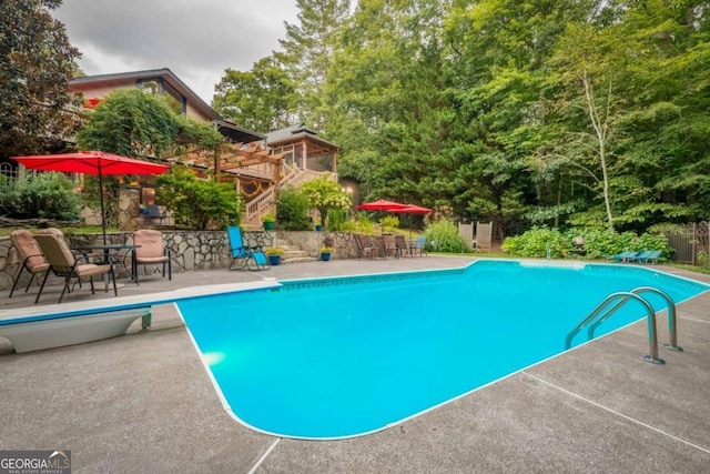 outdoor pool with a diving board and a patio area