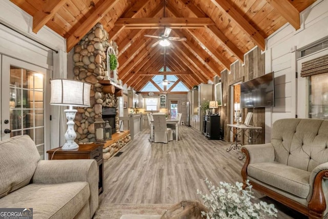 living area with a stone fireplace, beamed ceiling, wooden ceiling, and light wood-style flooring