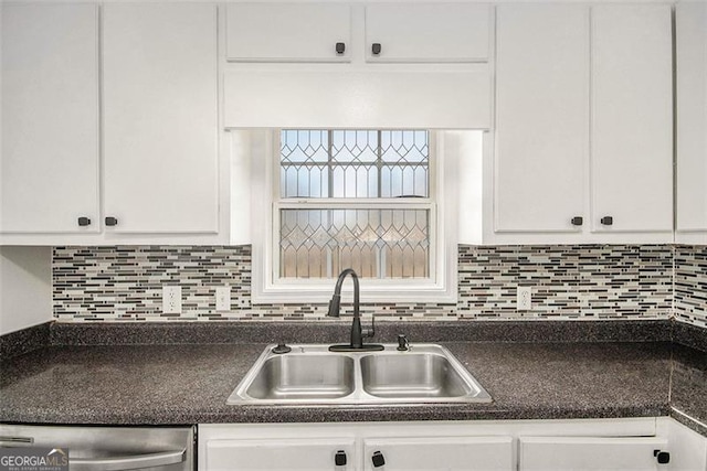 kitchen featuring decorative backsplash, white cabinets, dark countertops, a sink, and stainless steel dishwasher