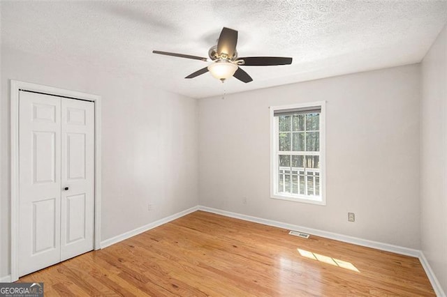 unfurnished bedroom with light wood finished floors, visible vents, baseboards, a textured ceiling, and a closet