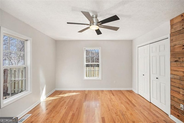 unfurnished bedroom featuring a textured ceiling, visible vents, baseboards, a closet, and light wood finished floors