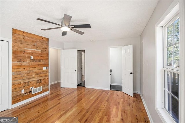 unfurnished bedroom with a textured ceiling, light wood-style flooring, a ceiling fan, visible vents, and baseboards