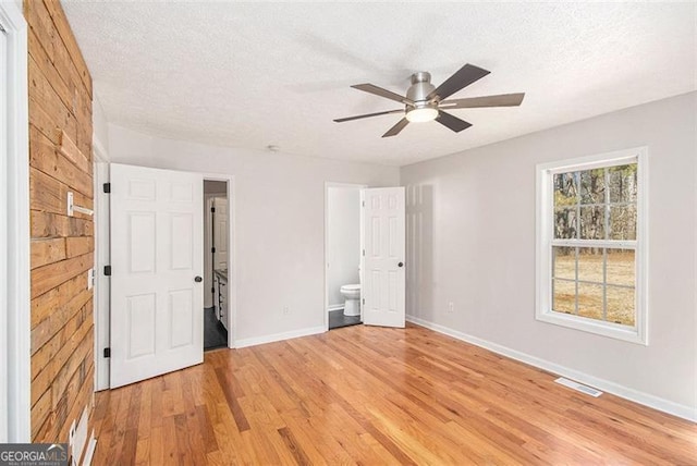 unfurnished bedroom featuring visible vents, a textured ceiling, ensuite bath, light wood-type flooring, and baseboards