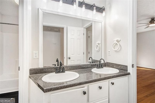 full bath with a ceiling fan, double vanity, a sink, and wood finished floors