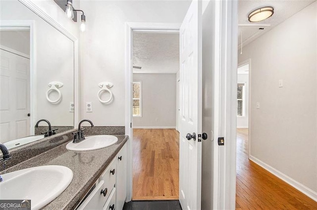 bathroom with double vanity, a textured ceiling, a sink, and wood finished floors