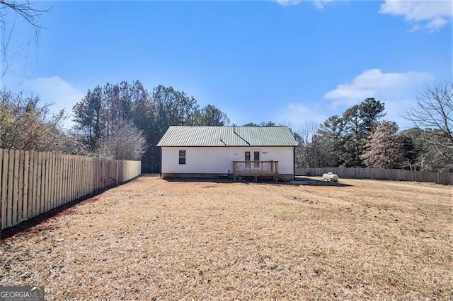 back of property featuring metal roof, a lawn, a fenced backyard, and a wooden deck