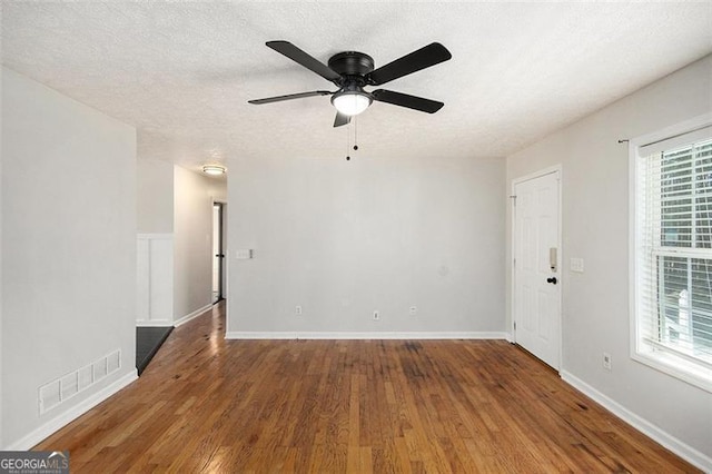 unfurnished room featuring a textured ceiling, visible vents, a wealth of natural light, and wood finished floors