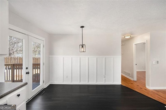 unfurnished dining area with a textured ceiling, french doors, dark wood finished floors, and visible vents