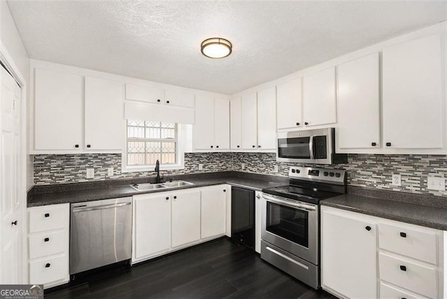 kitchen featuring stainless steel appliances, dark wood-style flooring, a sink, white cabinets, and dark countertops