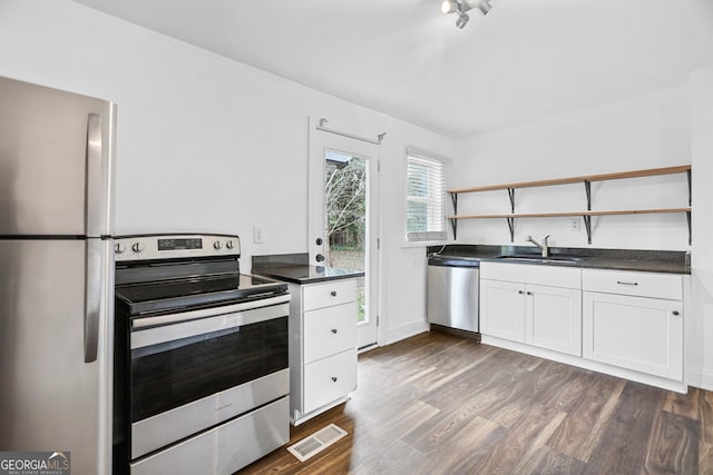 kitchen featuring dark countertops, appliances with stainless steel finishes, open shelves, and a sink